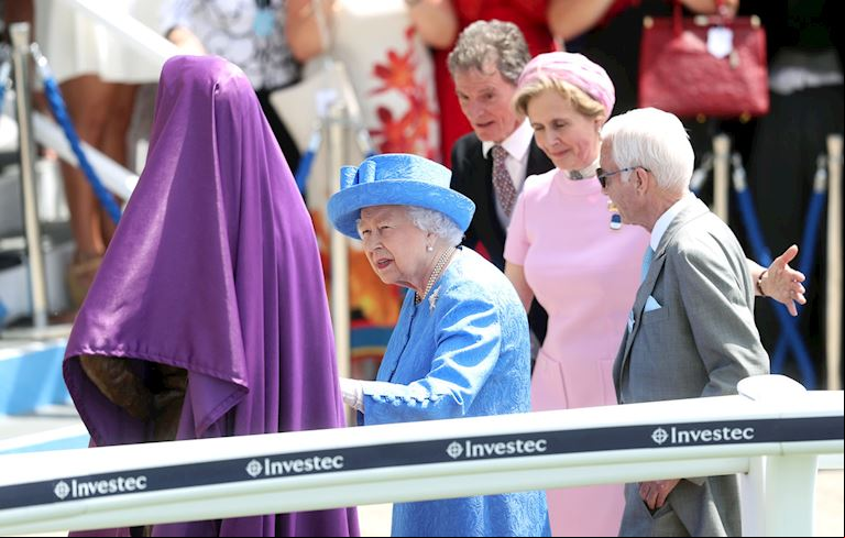 H.M The Queen removing a purple cloth to unveil a statue of Lestor Piggott, whilst wearing a blue outfit